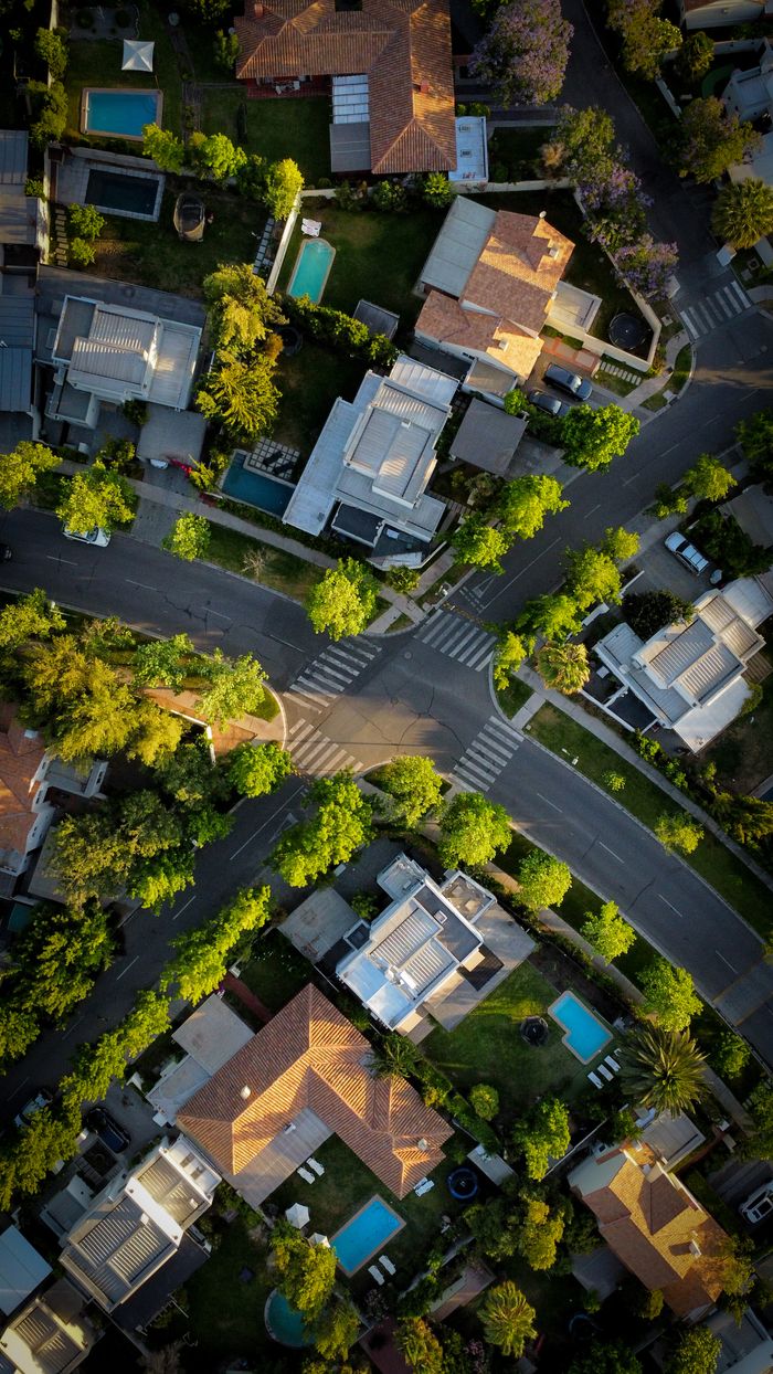 High-angle aerial view of an urban residential neighborhood with intersecting roads and green trees.