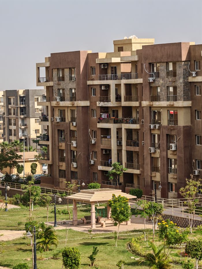 A tall residential apartment complex beside a lush green park on a sunny day.